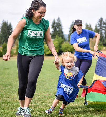 A volunteer holds the hand of a young girl who is playing outdoors.