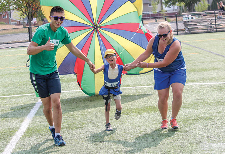 A volunteer and a staff member support a child with autism together in our Multisport summer day camp program.