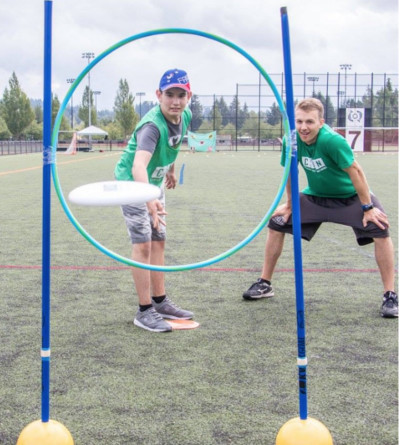 A child with autism throws a flying disc through a hoop under the guidance of a male volunteer.