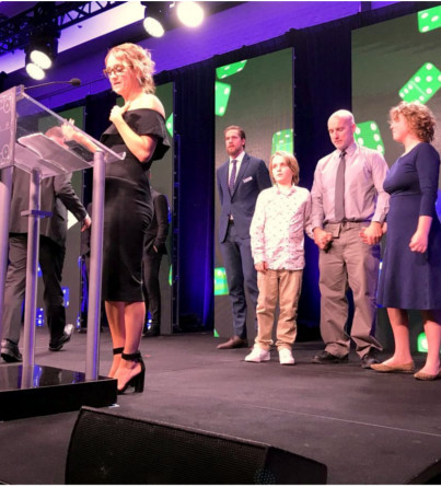 A woman speaks at a podium while her family stands behind her on stage.