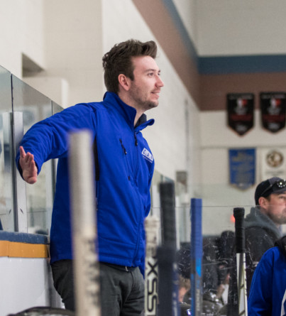 A male hockey coach stands on an arena bench.