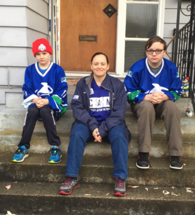 A mother and her two boys sit on their front porch steps wearing hockey jerseys.