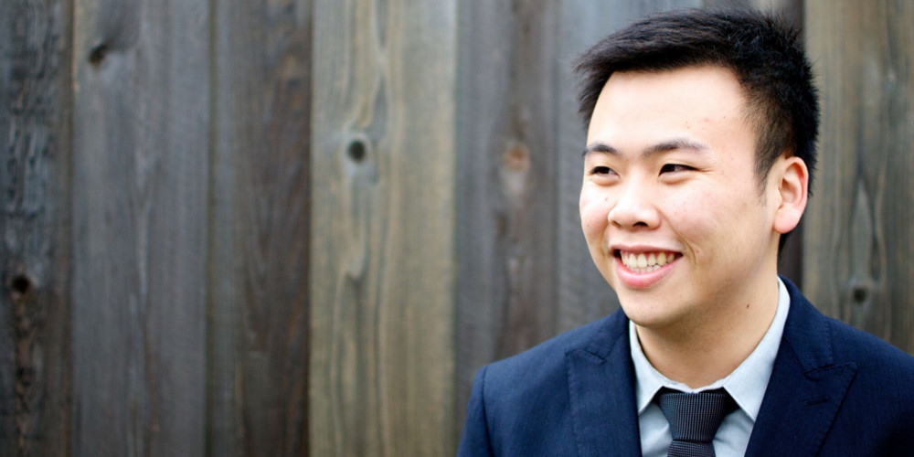 A male adult in a suit in front of a wood panel background