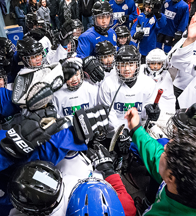 CAN ice hockey participants bring it in for a team cheer with coach.