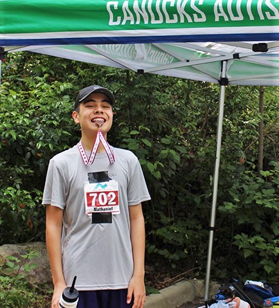 A male youth outfitted in running attire bites a racing medal in his mouth