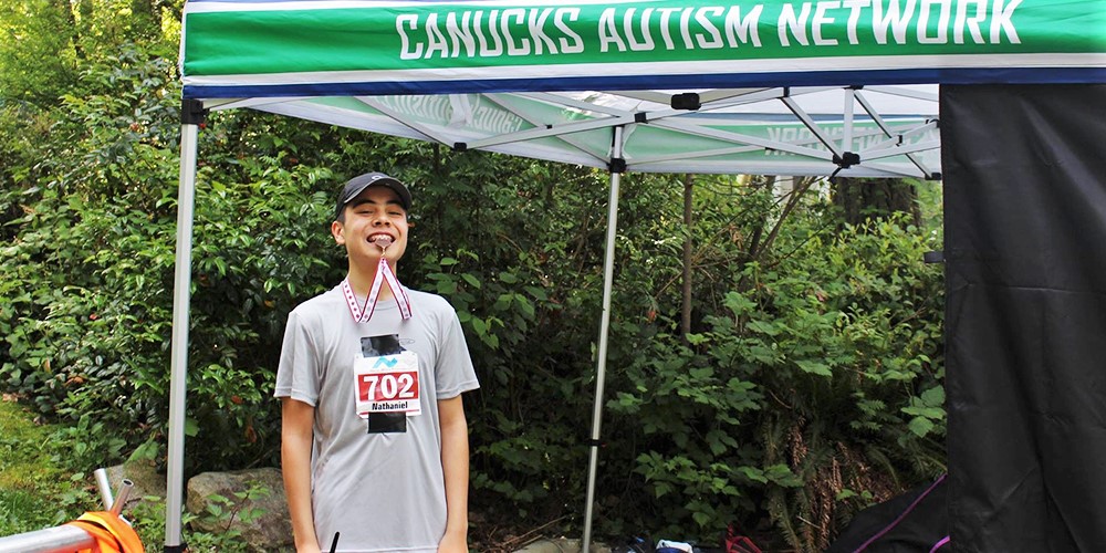 A male youth outfitted in running attire bites a racing medal in his mouth